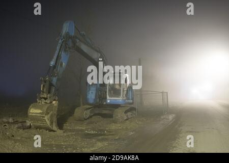 Blauer Bagger arbeitet nachts auf der Straße Stockfoto