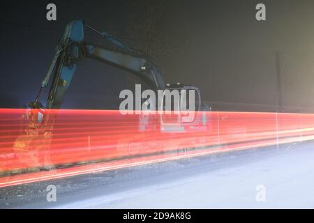 Blauer Bagger arbeitet nachts auf der Straße Stockfoto