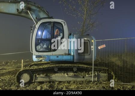 Blauer Bagger arbeitet nachts auf der Straße Stockfoto