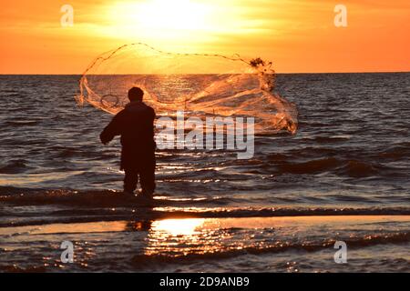 Fischer wirft sein Netz im Abendlicht im Tyrrenischen Meer bei Rom. Lebendige und beeindruckende Bild mit Mann in Hintergrundbeleuchtung und perfekte Netz. Stockfoto