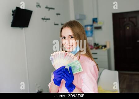 Weibliche Maniküre Meister im Schönheitssalon mit Schutzmaske halten Geld und Lächeln Stockfoto