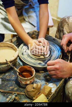 Die Hände eines Meisters und eines Studenten machen einen Krug auf einem Potter-Rad aus gelbem Ton. Selektive Fokussierung auf die Hände Stockfoto