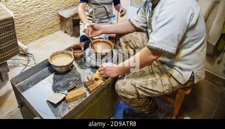 Die Hände eines Meisters und eines Studenten machen einen Krug auf einem Potter-Rad aus gelbem Ton. Selektive Fokussierung auf die Hände Stockfoto