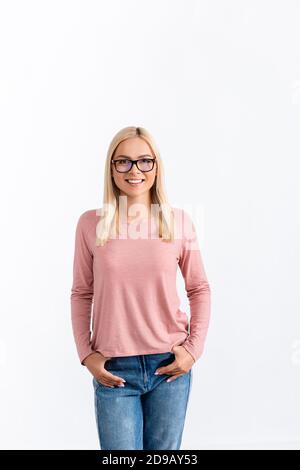 Vorderansicht einer lächelnden blonden Frau mit Händen in den Taschen, Brille und Blick auf die Kamera isoliert auf weiß Stockfoto