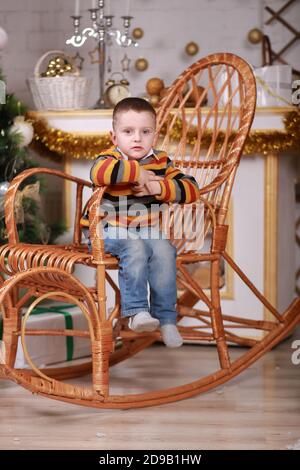 Niedlicher kleiner Junge sitzt in Schaukelstuhl in der Nähe von weihnachtsbaum Stockfoto