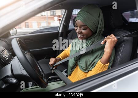 Fahrzeugsicherheit. Junge Schwarze Muslimische Dame In Hijab Befestigung Sitzgurt Im Auto Stockfoto