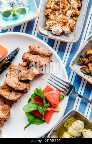 Gegrilltes Fleisch, Meeresfrüchte, Meze, Kräuter, Fisch, Raki, Ouzo, Vorspeisen und Salate im griechischen oder türkischen Restaurant auf dem Tisch zum Abendessen oder Mittagessen am Strand Stockfoto