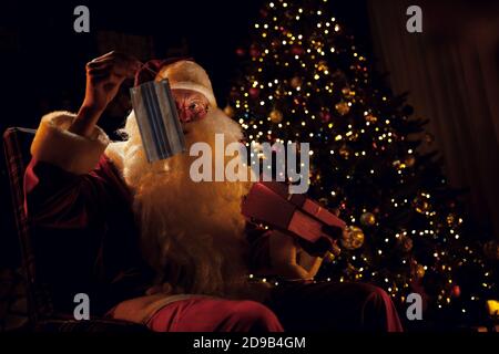 Überrascht Santa zieht aus einem Geschenk eine medizinische Maske und versteht nicht, was mit ihm zu tun. Stockfoto