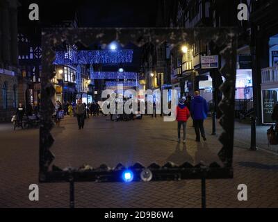 Weihnachtseinkäufer am späten Abend, umrahmt von einer Buskerrequisite auf der historischen Eastgate Street in Chester, England Stockfoto