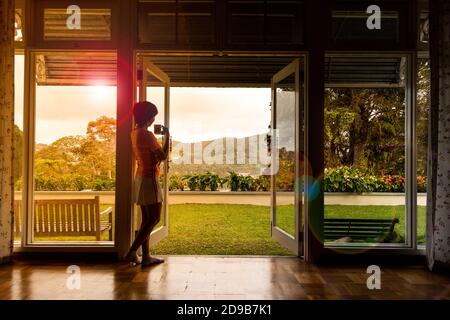 Frau bewundern natürliche szenische Sonnenaufgang von zu Hause aus mit Kaffee Stockfoto