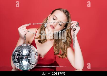 Junge Frau hält Kette in der Nähe glänzend Disco Ball auf rot Stockfoto