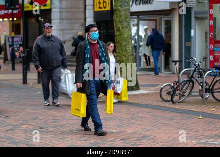 Birmingham, Großbritannien. November 2020. Ein Gentleman trägt einen Schal, während er Taschen von Selfridges trägt, während das Land morgen in einen anderen Lockdown Gerät. Das Wetter ist frisch und kühl. Kredit: Ryan Underwood/Alamy Live Nachrichten Stockfoto