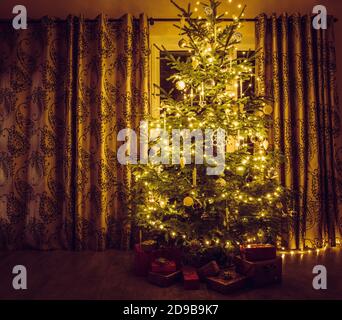 Weihnachtsbaum mit warmen gelben Sehnenleuchten und weißen Eiszapfen und Schneeflocken-Form Ornamenten. Rot verpackte Geschenke unter dem Baum. Stockfoto