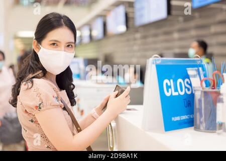 Asiatische Frau mit Hygiene Gesichtsmaske vor der Kasse im Flughafen stehen. Selbstschutz während des COVID-19 oder Coronavirus-Ausbruchs durch USI Stockfoto