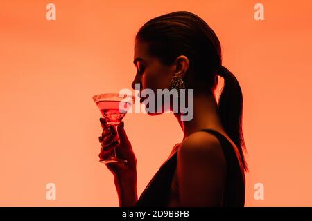 Seitenansicht der jungen Frau, die margarita Cocktail mit Eis hält Würfel auf Orange Stockfoto