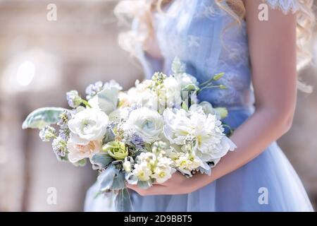 Eine Braut in einem blauen Hochzeitskleid hält einen Hochzeitsstrauß in ihren Händen. Großer schöner Brautstrauß aus weißen Rosen und Pfingstrosen Stockfoto