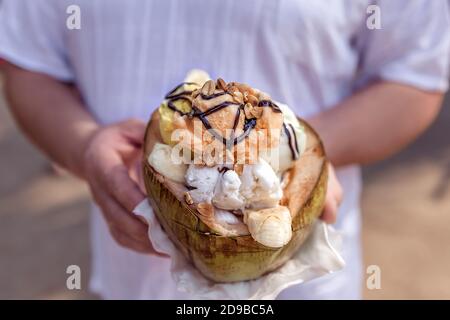 Nüsse und Banane mit Schokolade Belag auf Eis. Eis in einer Kokosnuss in den Händen halten. Nahaufnahme. Stockfoto