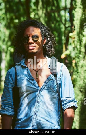 Musiker, der mit der Gitarre auf dem Rücken hängt. Er läuft in einem Park mit Vegetation. Stockfoto