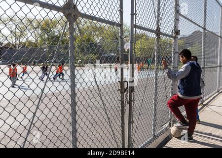 NEW YORK, USA - 27. Apr 2016: Jungs beobachten die Kinder beim Fußballspielen auf dem Kinderspielplatz in Brooklyn, New York City Stockfoto