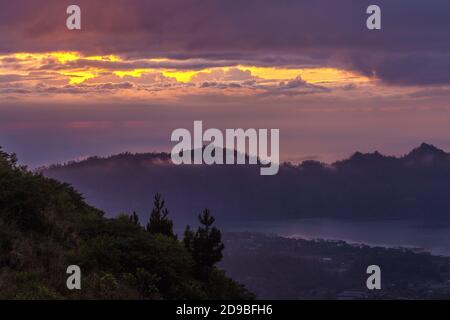Herrlicher Panoramablick auf die Natur von der Spitze des Vulkans Batur bei Sonnenaufgang, Bali. Luftaufnahme auf Berg, lila Himmel und See am nebligen Morgen Stockfoto