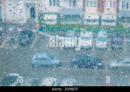 Blick durch ein regnerisches Fenster auf ein verschwommenes Haus und Parkplatz. Konzept für schlechtes Regenwetter. Stockfoto