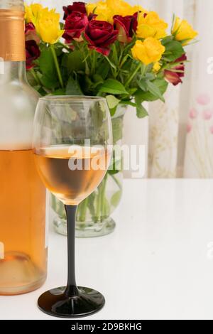 Nahaufnahme von gefülltem Weinglas in der Nähe der Flasche und farbenprächtiges Rot Und gelbe Rosen Blumen in Vase als romantische Feier Abendessen Konzept Stockfoto