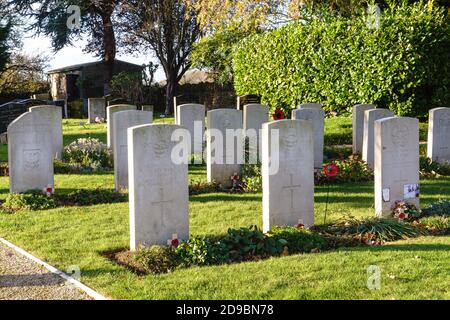 Kidlington, Oxfordshire, Großbritannien, 4. November 2020. Die Sonne geht auf Gräbern unter, die mit roten Mohnblumen und Kreuzen von Gemeindemitgliedern geschmückt sind und auf der Commonwealth war Graves-Stätte hinter der St. Mary's Church in Kidlington ausgestellt sind. Es gibt 25 Gräber im Kidlington Friedhof und 3 Gräber im Kirchhof. Die Gedenkfeiertage wurden in diesem Jahr aufgrund der Coronavirus-Pandemie eingeschränkt. Bridget Catterall/Alamy Live News. Stockfoto