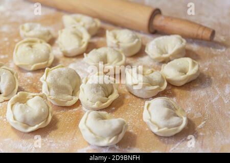 Nahaufnahme von halbfertigen Pelmeni-Knödeln auf dem Holzbrett. Stockfoto