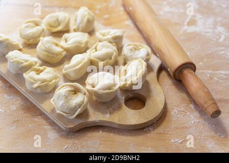 Nahaufnahme von halbfertigen Pelmeni-Knödeln auf dem Holzbrett. Stockfoto