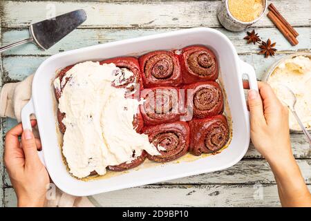 Hausgemachte Zimtrollen roten Samt mit Frischkäse Glasur auf weißem Holzhintergrund, Draufsicht Stockfoto