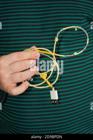 Das Kind hält ein altes zerrissenes USB-Kabel in der Hand. Nahaufnahme Stockfoto