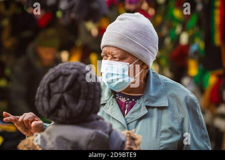 London, Großbritannien - 3. November 2020 - EINE ältere schwarze Frau, die eine Gesichtsmaske trägt, während sie mit ihrem Freund auf dem Walthamstow-Markt spricht Stockfoto