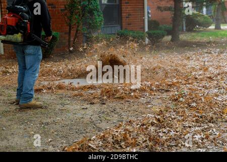 Mann, der den Bürgersteig mit einem Laubgebläse reinigt Herbst Stockfoto