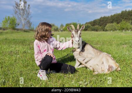 Kind Mädchen liebevoll berühren Ziege auf Gras auf der Wiese liegen Stockfoto