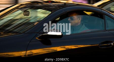 Belgrad, Serbien - 9. Oktober 2020: Reifer Mann in Anzug mit Sonnenbrille fahren ein schwarzes Auto auf der Stadtstraße, allein, durch das Fenster mit Reflexen Stockfoto