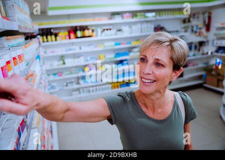 Kaukasische Frau, die durch Drogerie sucht, um Medikamente für kranke Tochter zu finden. Spaziergang durch die Apotheke Stockfoto