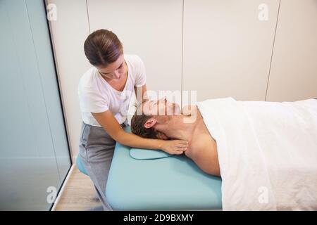 Weibliche Physiotherapeutin, die Kopfmassage für den männlichen Patienten gibt Stockfoto