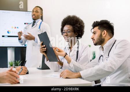 Nahaufnahme Porträt von zwei jungen Ärzten, Afrikanerin und Inder, sitzen am Tisch und diskutieren medizinischen Fall. Schöner afrikanischer männlicher Arzt Stockfoto