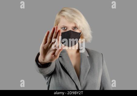 Junge blonde Frau in schwarzer medizinischer antiviraler Maske schaut auf die Kamera. Hand nach vorne, stoppen Coronavirus Stockfoto