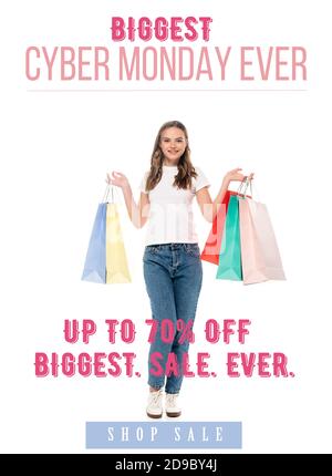 Fröhliche junge Frau hält bunte Einkaufstaschen und schaut zu Kamera in der Nähe größte Cyber monday jemals Schriftzug auf weiß Stockfoto