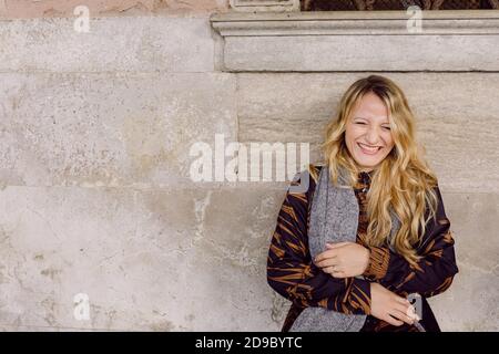 Schönes Mädchen mit einem schwarzen und braunen Kleid und einem grauen Schal, auf einer Bank sitzend und lachend in Venedig, Italien Stockfoto