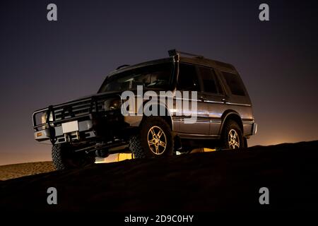 Ein nicht identifizierbarer SUV steht auf einer Sanddüne im Wüstenuntergang in den Vereinigten Arabischen Emiraten Stockfoto