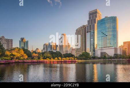 Stadtpark mit See unter Wolkenkratzern bei Sonnenaufgang. Benjakiti Park in Bangkok, Thailand Stockfoto
