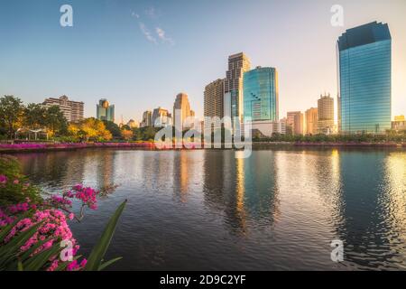 See mit violetten Blumen im City Park unter Wolkenkratzern bei Sonnenaufgang. Benjakiti Park in Bangkok, Thailand Stockfoto