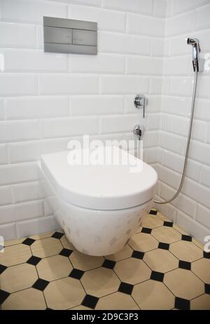 Ein im Retro-Stil renovierter Toilettenraum mit weiß gefliesten Wänden, gelben und schwarzen Vintage-Bodenfliesen, einer an der Wand montierten Keramik-Toilettenschüssel und einem handgehaltenen Bidet Stockfoto
