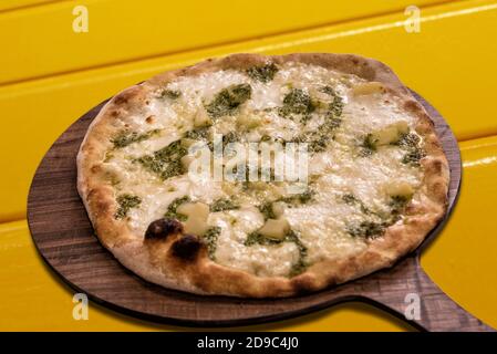 Pizza mit genuesischem Pesto, Kartoffeln und Mozzarella-Käse auf Holzschneidebrett auf gelbem Hintergrund Stockfoto