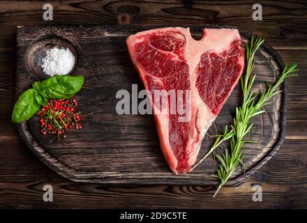 Rohes Porterhouse Steak, trocken gereift auf Holzbrett mit Kräutern, Pfeffer und Salz Stockfoto