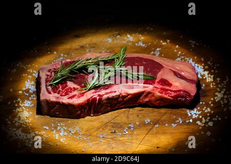 Rohes Steak liegt im Dunkeln auf einem Kochbrett Und beleuchtet durch Lichtstrahl Stockfoto