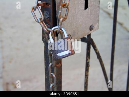Ein neues braunes Vorhängeschloss mit einem glänzenden Bogen hängt an einer Kette an einer eisernen Tür. Stockfoto