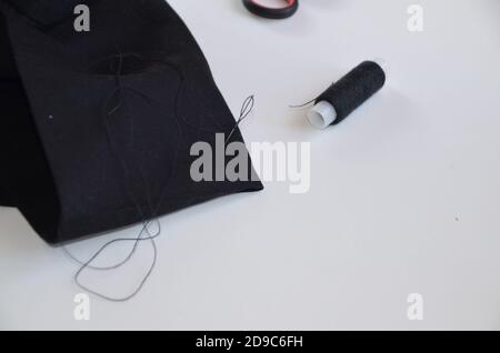 Mädchen näht mit Faden und Nadel schwarz Material. Saum Hose. Verdreht den Faden zu einer Nadel. Schneider Mann arbeitet in seinem Schneider-Shop, Schneiderei Stockfoto